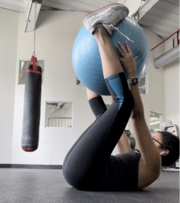 Deepti Sharma laying on the floor for a workout routine with a blue medicine ball