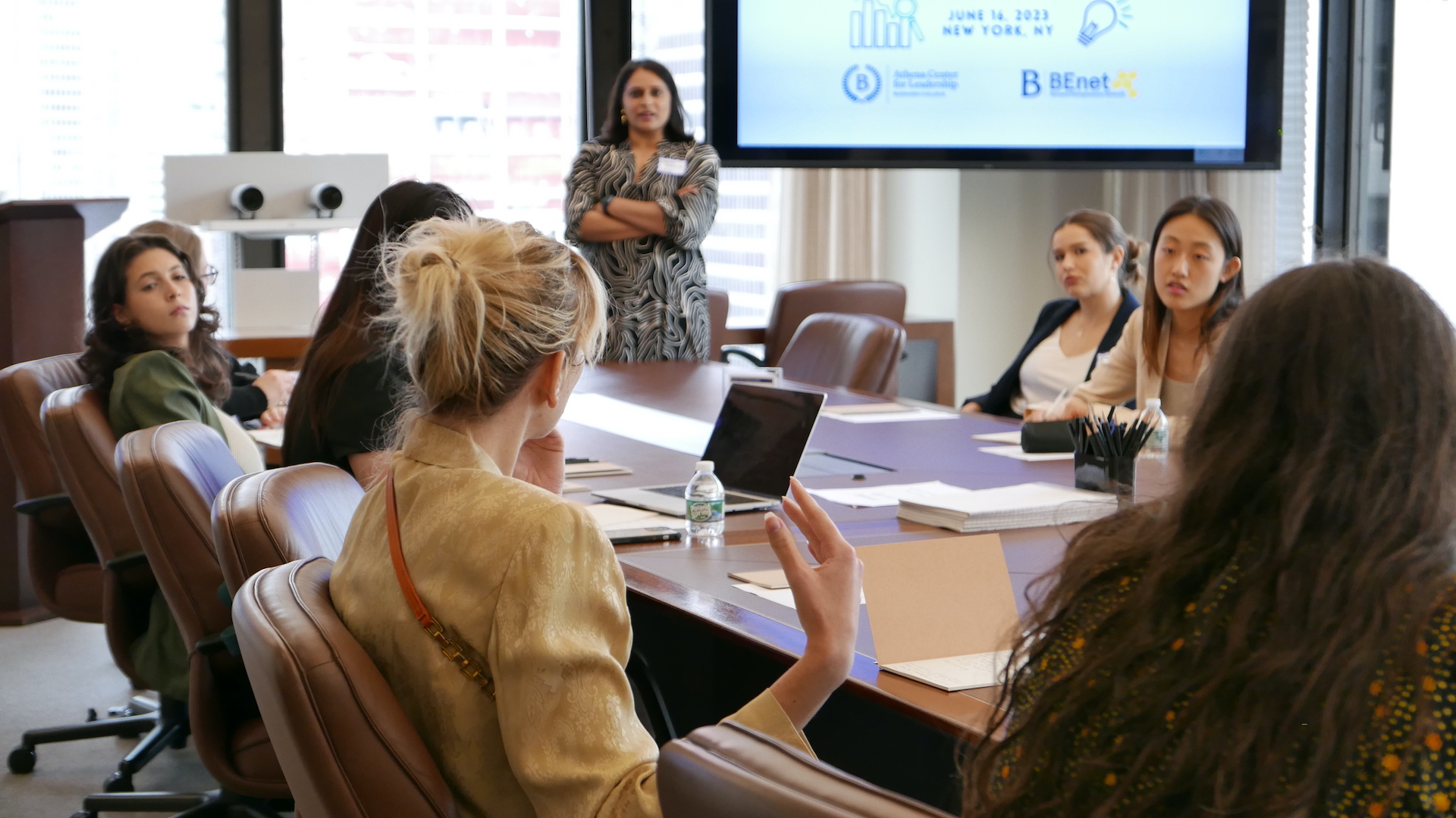 [Image description: a group of Barnard entrepreneurs sitting around a conference table. A blonde woman is in focus with her back to the camera and is gesturing with her right hand. Umbreen Bhatti '00 is blurred in the distance, leading the discussion.]