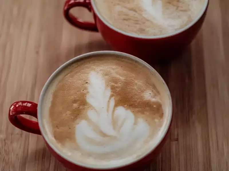 [Image description: two red mugs with coffee latte art on a wooden table.]