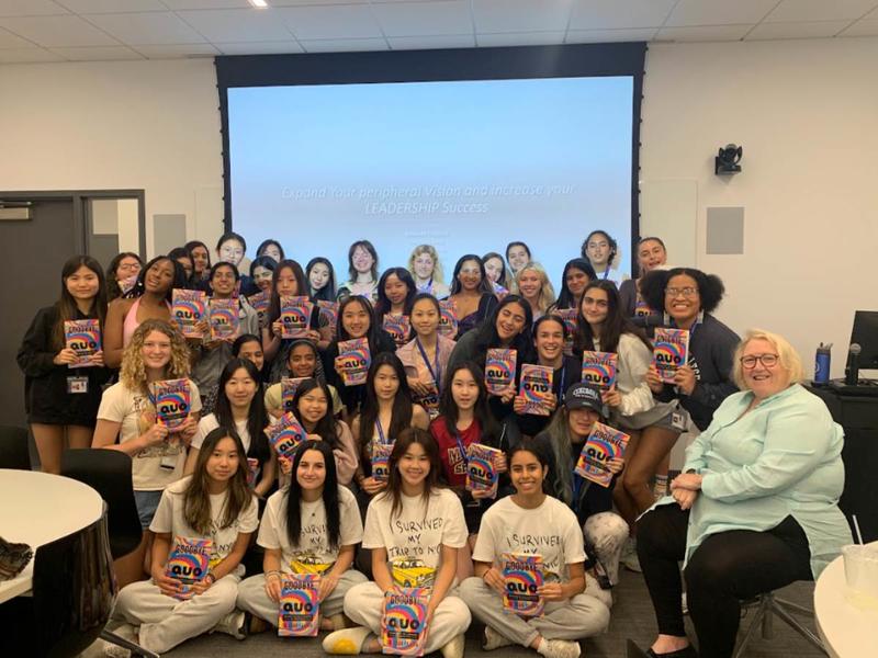 [Image description: The 2023 ASII cohort with Joan Fallon, author of "Goodbye, Status Quo", which all students have in their hands. Students are standing in front of a screen with the words "Expand your peripheral vision and increase your LEADERSHIP success" projected.]