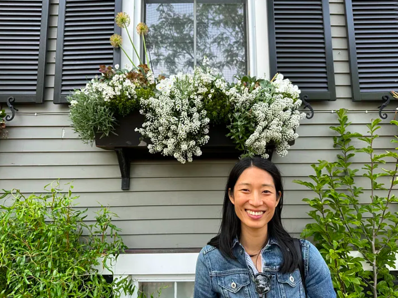 [Image description: Amy Chen in from of a house with foliage behind her]